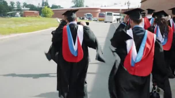 Groupe d'étudiants diplômés marchant le long du bâtiment en brique rouge — Video