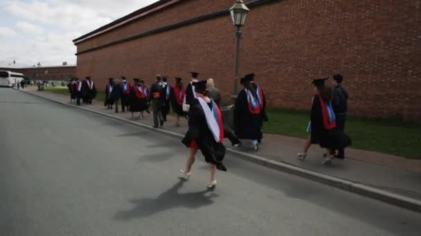 Группа выпускников, идущих вдоль стены из красного кирпича — стоковое видео