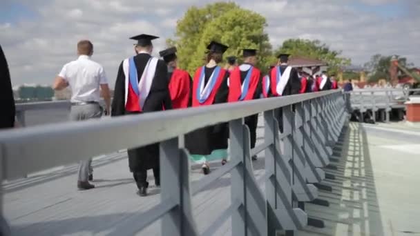 Grupo de estudiantes graduados caminando en el puente de madera al aire libre en — Vídeo de stock