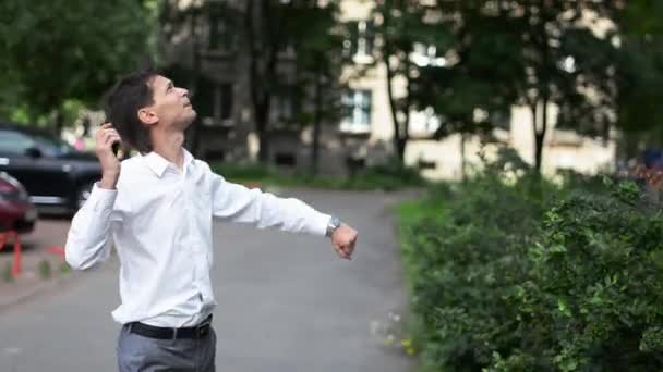 Homme en chemise blanche debout sous les fenêtres de la maison avec téléphone, il chante et danse . — Video