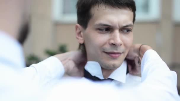 Someone helps man in white shirt wear a tie, while man talk on phone. — Stock Video