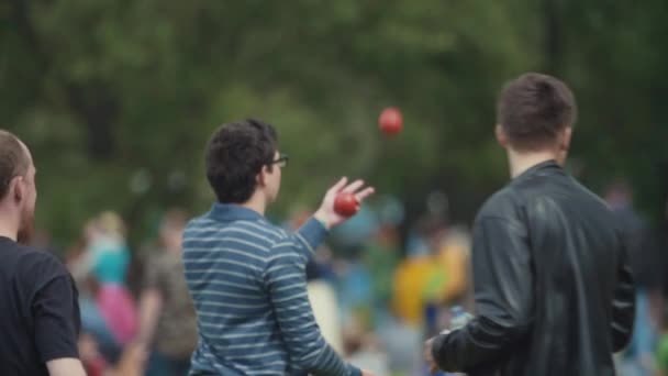 Zeitlupenmann mit Brille joggt im Sommer im Stadtpark rote Bälle — Stockvideo