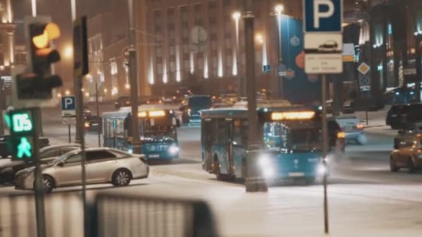 Two blue shuttle buses rides down night city street in falling snow — Stock Video