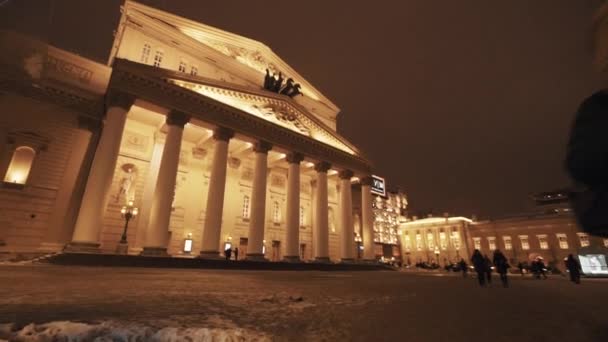 Пешеходы проходят мимо здания театра в зимнюю ночь — стоковое видео