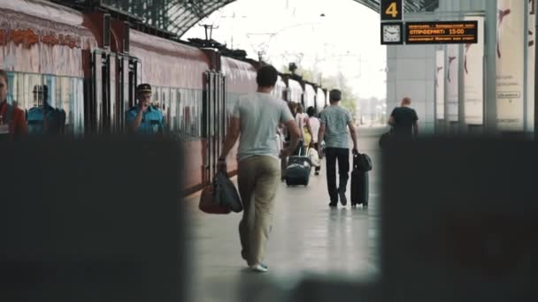 Пассажиры с сумками идут вдоль красного поезда по железной дороге — стоковое видео