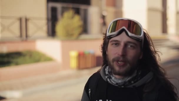 Bebaarde snowboarder met lange haren lopen op straat en geven inter — Stockvideo