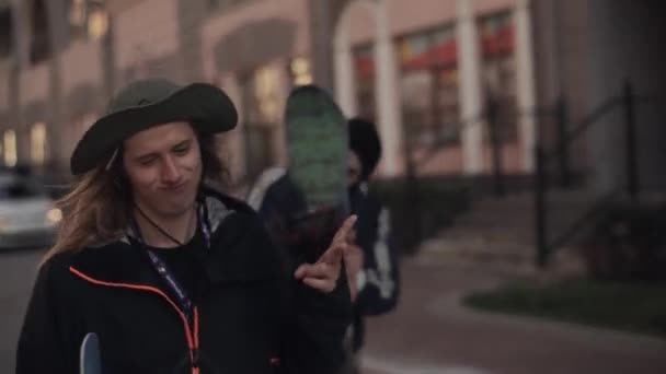 Mladých snowboardistů s dlouhými vlasy v klobouku chodit na ulici a dát — Stock video