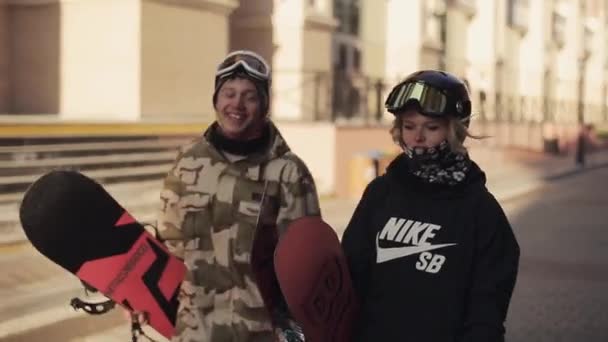 Jeune couple de snowboarders avec de longs cheveux marcher sur la rue et g — Video