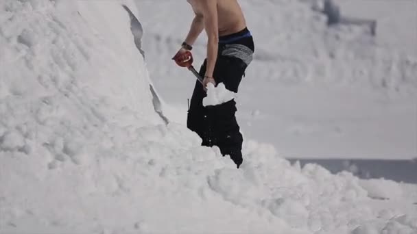 Гірськолижний курорт. Красива людина в сонцезахисних окулярах додає снігу, що душ на схилі лопатою. Гори. Сонячний день — стокове відео