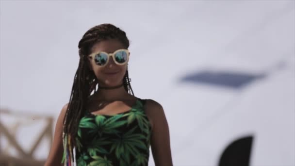 Lyžařské středisko. Dívka v brýle, zelené tričko s africkými COP úsměv ve fotoaparátu. Hory. Slunečný den — Stock video