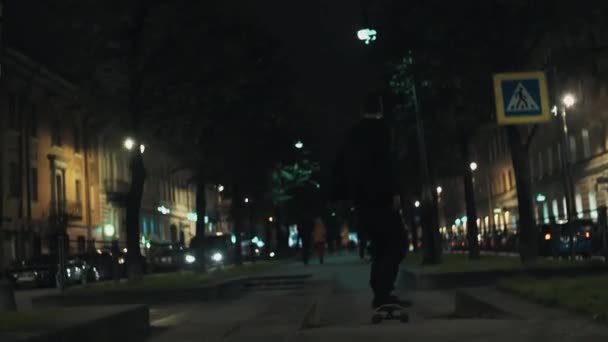 Skateboarder hombre en negro sudadera con capucha paseos en nigth city park alley — Vídeos de Stock