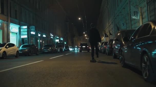 Skateboarder guy in black hoodie rides on night city road — Stock Video