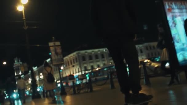 Skateboarder uomo con cappuccio nero cavalca sulla affollata città notturna foo — Video Stock