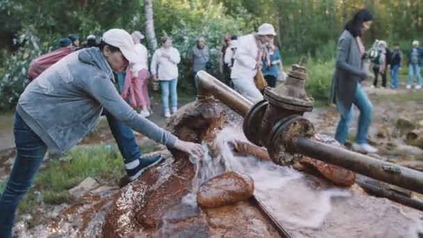 Mulher enchendo garrafa com água de tubulação enferrujada na floresta, multidão de pessoas — Vídeo de Stock