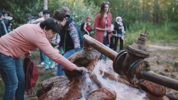 Mulher enchendo garrafa com água da nascente na floresta, multidão de pessoas — Vídeo de Stock