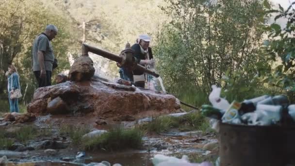 Pareja mayor llenando botellas de manantial oxidado en bosques llenos de basura — Vídeos de Stock