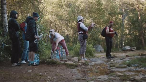 People queue to waterspring to fill up bottles at mountain trail — Stock Video