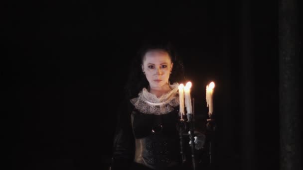 Femeia mistică în rochie victoriană holbându-se în cameră întunecată cu candelabru — Videoclip de stoc