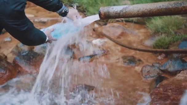 Man pours water into bottle water from wellspring on woods mountain trail — Stock Video