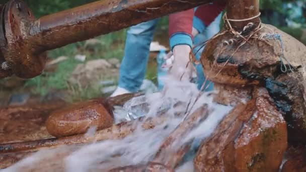Человек наливает воду в бутылку из природного источника на лесной горной тропе — стоковое видео