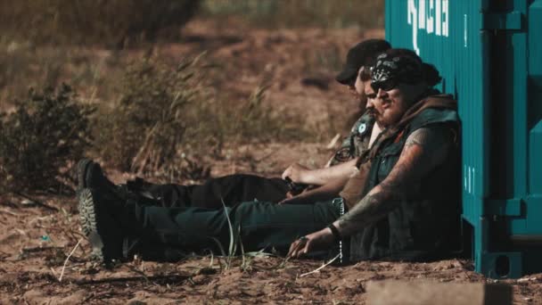 Grupp av rocker män sitter på marken lutar på Last container — Stockvideo