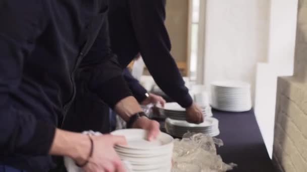 Camera shows several pairs of hands put bunch of white plates on dark table — Stock Video