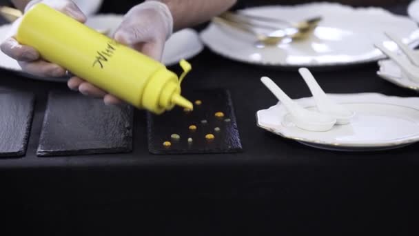Dekorieren schwarzer rechteckiger Teller, indem Tropfen aus einer gelben Plastikflasche aufgesetzt werden — Stockvideo