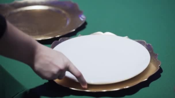 Vrouwen handen plaatsen witte borden op tafel met groen tafelkleed — Stockvideo