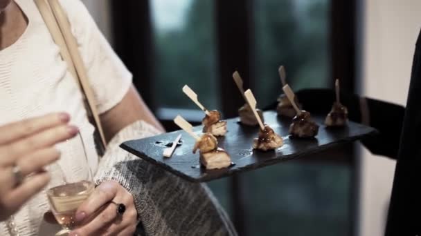 Femme en vêtements légers essaie des collations sur plateau offert par le serveur en uniforme noir .