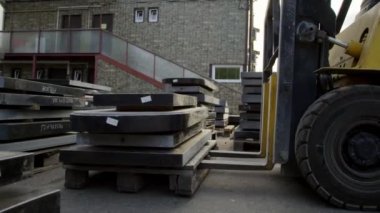 Koyu granit bloklarla yüklü sarı pallet kaldırıcı görüntüsü engelleri kaldırıyor.