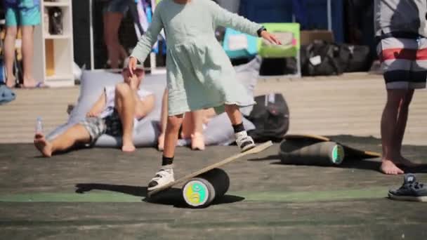 MOSCÚ, RUSIA - 12 de julio de 2019: Una niña sonriente vestida de blanco se para en el tablero de equilibrio y mira a la cámara — Vídeos de Stock