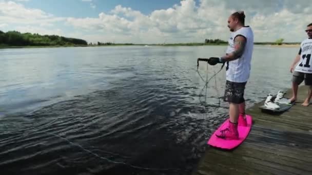 MOSCÚ, RUSIA - 12 DE JULIO DE 2019: El hombre de camiseta blanca y pantalones cortos está en el tablero acuático listo para comenzar el esquí acuático — Vídeo de stock