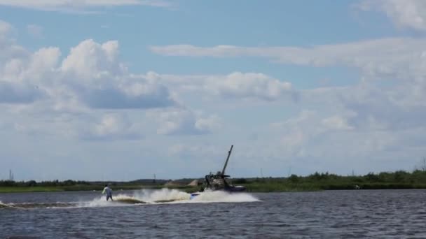 MOSCÚ, RUSIA - 12 DE JULIO DE 2019: Joven macho monta juguetonamente esquí acuático a la velocidad siguiente barco de motor a lo largo del río — Vídeos de Stock