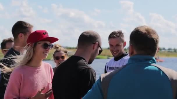 МОСКВА, РОССИЯ - 12 июля 2019 года: группа симпатичных молодых людей в красочной одежде тусуется на пирсе неподалеку от реки — стоковое видео