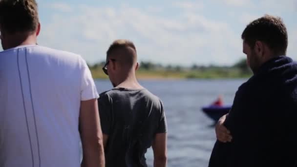 Moskou, Rusland - 12 juli 2019: Een aantal actieve jongemannen staan voor de rivier en kijken naar drijvende motorboten — Stockvideo