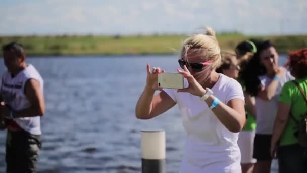 Moskva, Rusko - 12. července 2019: Starší blondýnka fotí na kameře smartphone poblíž řeky — Stock video