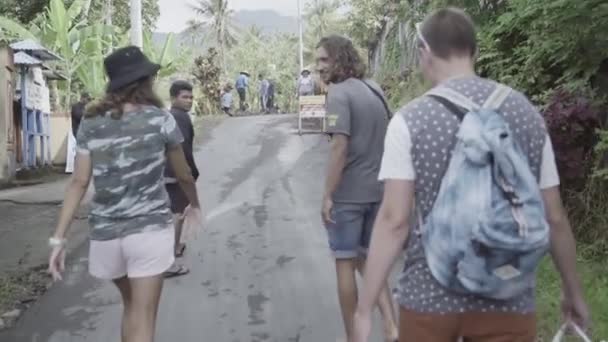 Bali, Indonezja - 22 kwietnia 2018: Trzech turystów spaceruje po azjatyckiej wsi z miejscową ludnością w upalny dzień. — Wideo stockowe