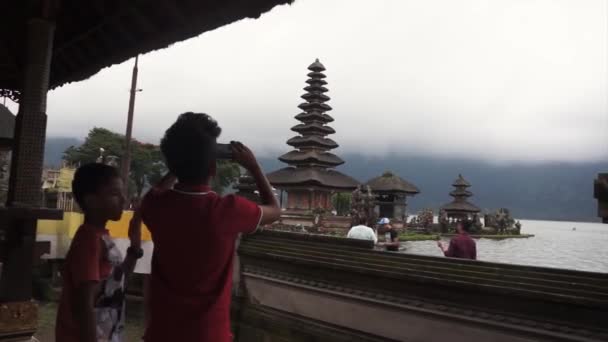 BALI, INDONÉSIA - 22 de abril de 2018: Meninos tiram fotos de Pura Ulun Danu Bratan, grande templo aquático de Bali, Indonésia — Vídeo de Stock