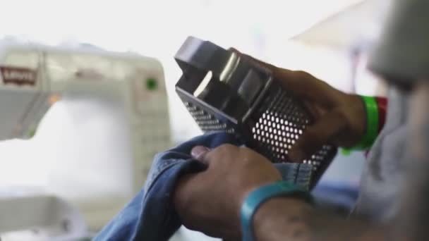 Man arms making decorative tears with food grater on denim jeans — Stock Video