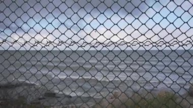 Güzel sahil şeridindeki metalik ağ boyunca dalgaların kıyılara düşüşünü izle.