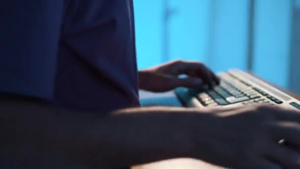 Guy in t-shirt si siede alla scrivania, digitando sulla tastiera nera poi prendendo smartphone . — Video Stock