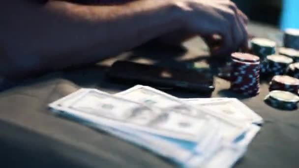 Homme en t-shirt assis au bureau couvert de billets en dollars américains et de jetons de casino .