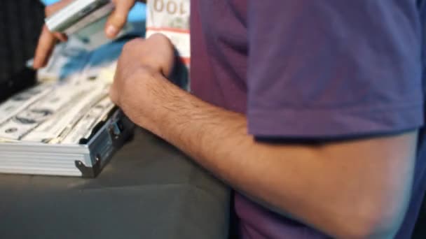 Ώριμος άνδρας σε t-shirt μας βάζει δολάρια και άλλα νομίσματα σε μεταλλική βαλίτσα. — Αρχείο Βίντεο