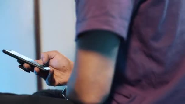 Slim mâle en t-shirt violet se trouve dans la chambre noire et activement en utilisant son smartphone .