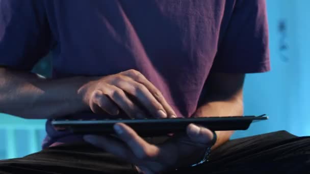 Cara magro está sentado no quarto escuro e digitando ativamente no teclado portátil . — Vídeo de Stock