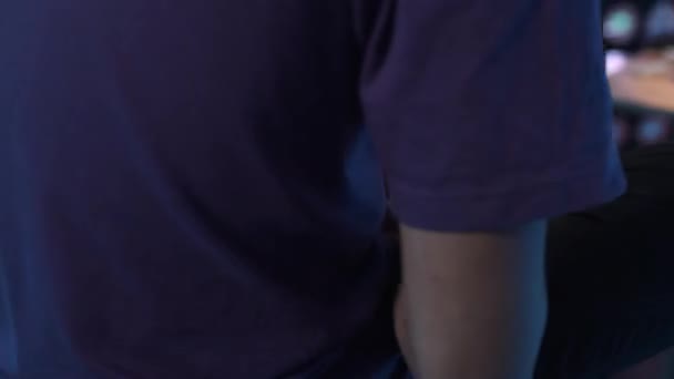 Slim macho en camiseta violeta se sienta solo en la habitación oscura y usando su teléfono inteligente . — Vídeos de Stock