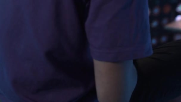 紫のTシャツの若い男は暗い部屋に一人で座って、彼の携帯電話を使用しています. — ストック動画