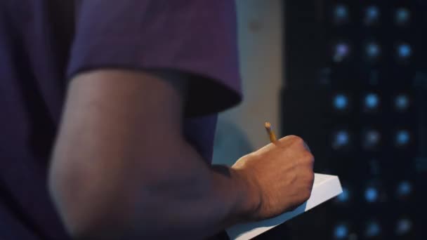 Guy in violet t-shirt sits in room with blue walls, does writing in notebook — Stock Video