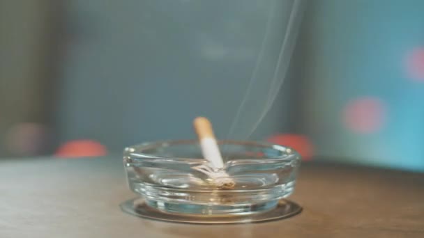 Turning around glass ash tray with burning cigarette placed on its edge in room. — Stock Video