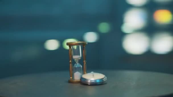 Изолированные ручные часы и песочные часы, расположенные на темном круглом столе в комнате . — стоковое видео